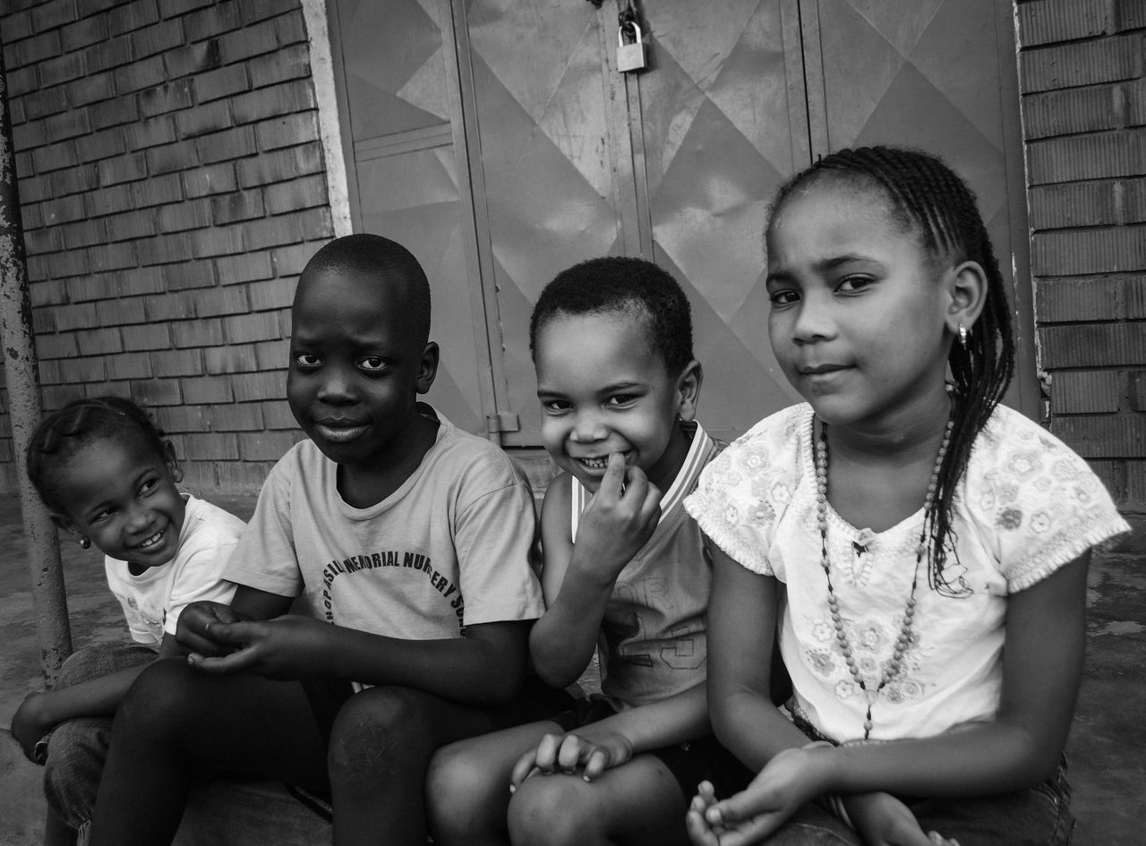 A group of smiling children sitting together outdoors in a black and white photograph.