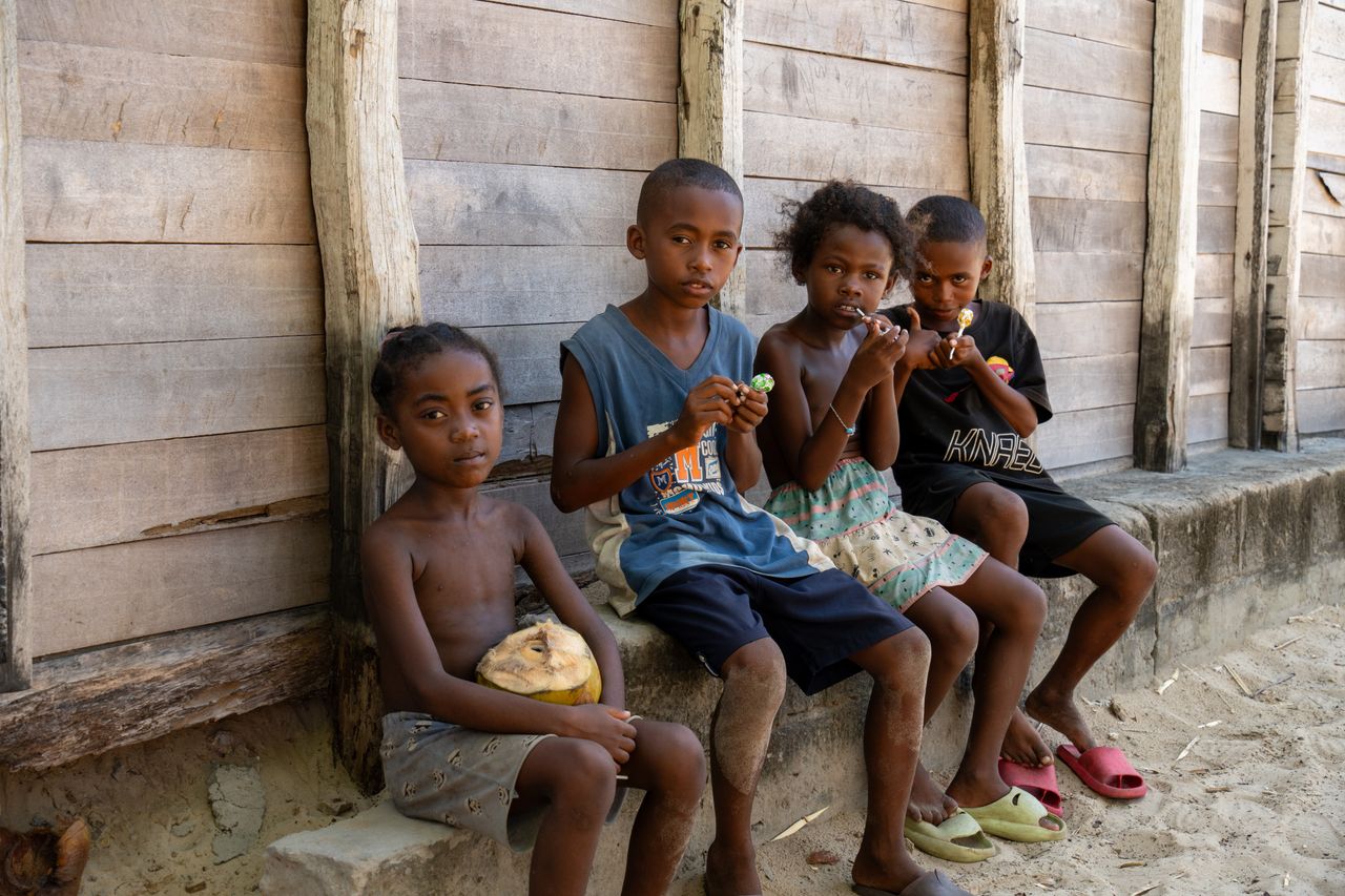 Four children eating lollipops sit by a wooden building in Madagascar.