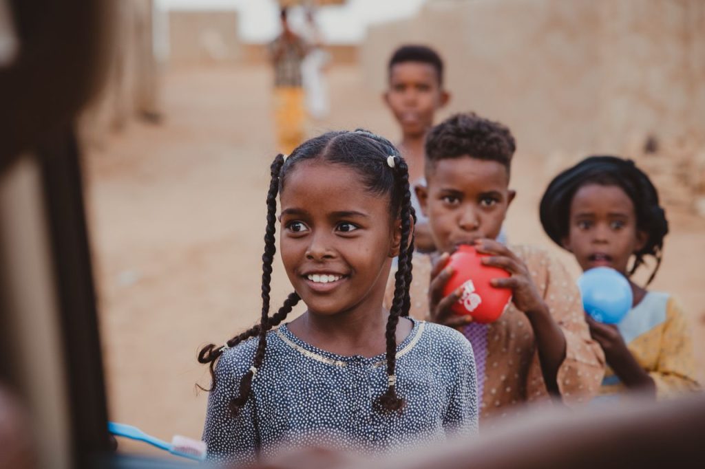 Group of smiling children playing with colorful balloons in a rural setting, embracing simple joys.