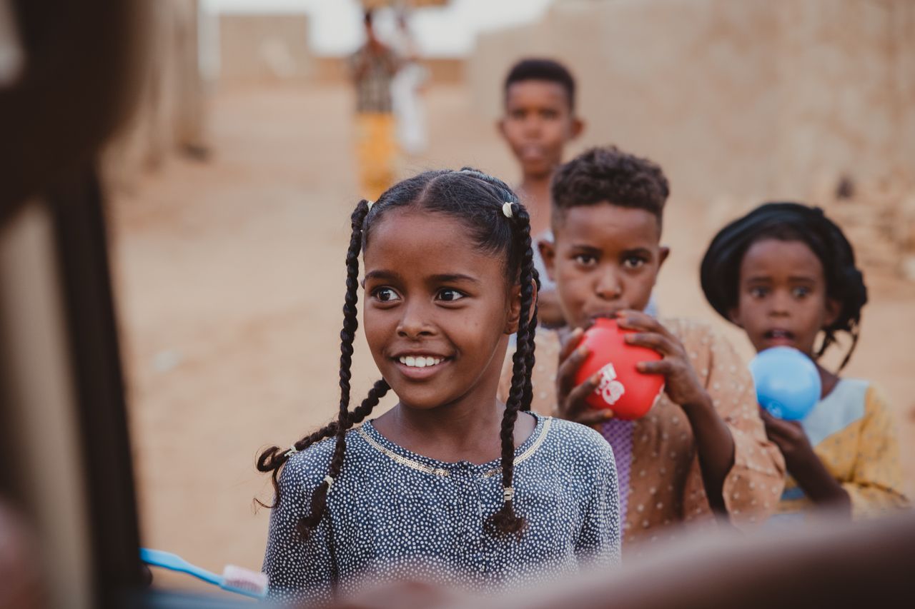 Group of smiling children playing with colorful balloons in a rural setting, embracing simple joys.