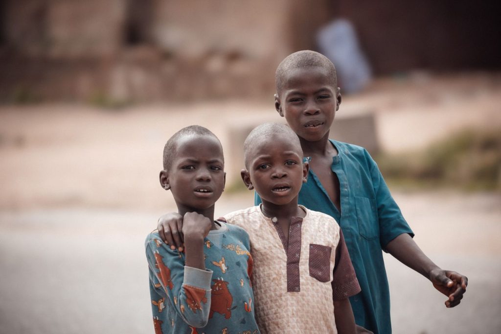 Portrait of three young boys smiling and posing outdoors in Bauchi, Nigeria.